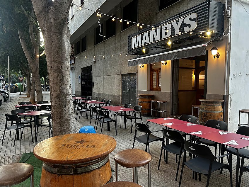 Terraza de Manbys por la noche: mesas en la acera y el rótulo luminoso